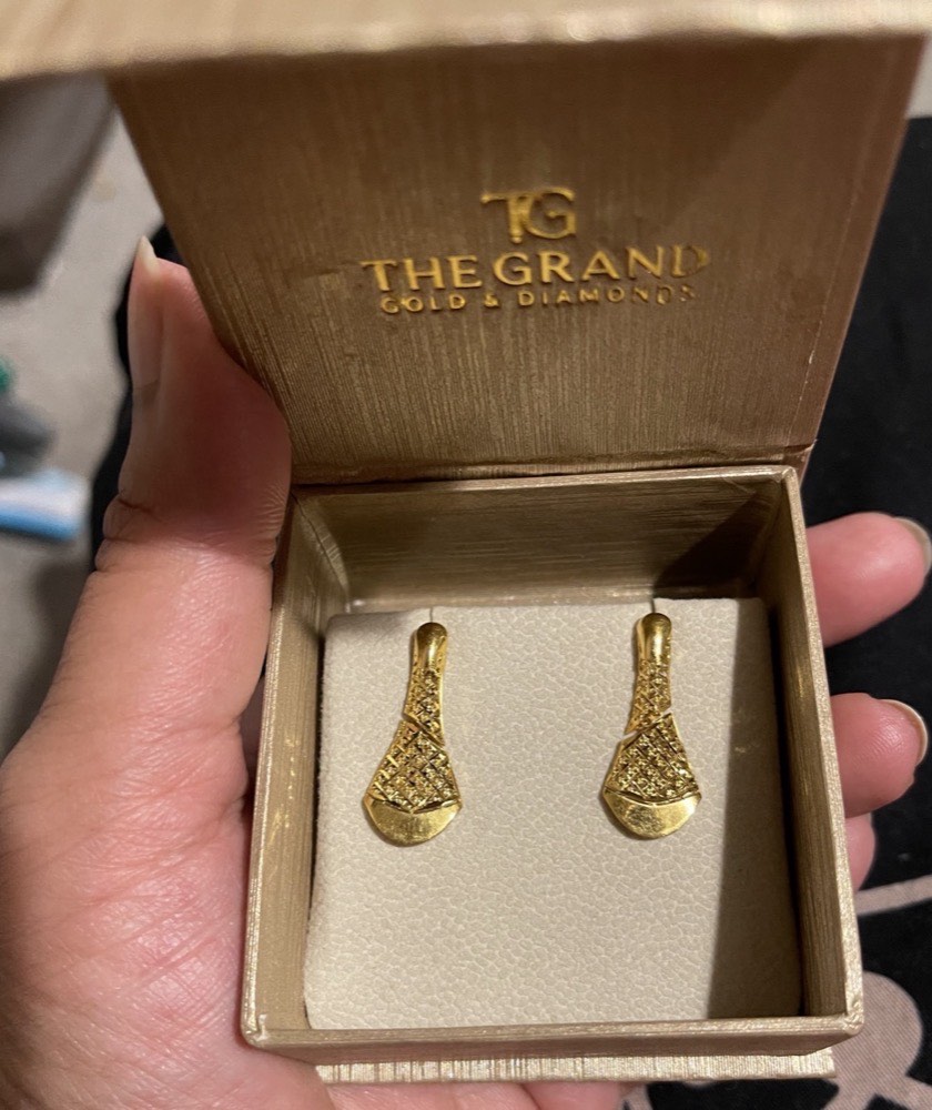 A pair of gold earrings in a branded The Grand Gold and Diamonds presentation box, held out to show the detail